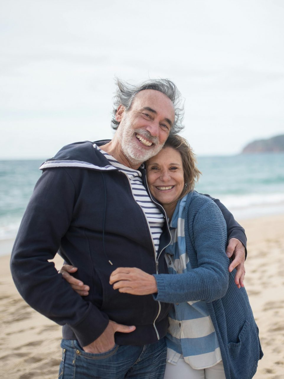 Happy senior couple embracing on a sandy beach in Portugal, symbolizing love and togetherness.