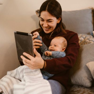 A mother and baby video calling at home, sharing a joyful moment on a cozy bed.